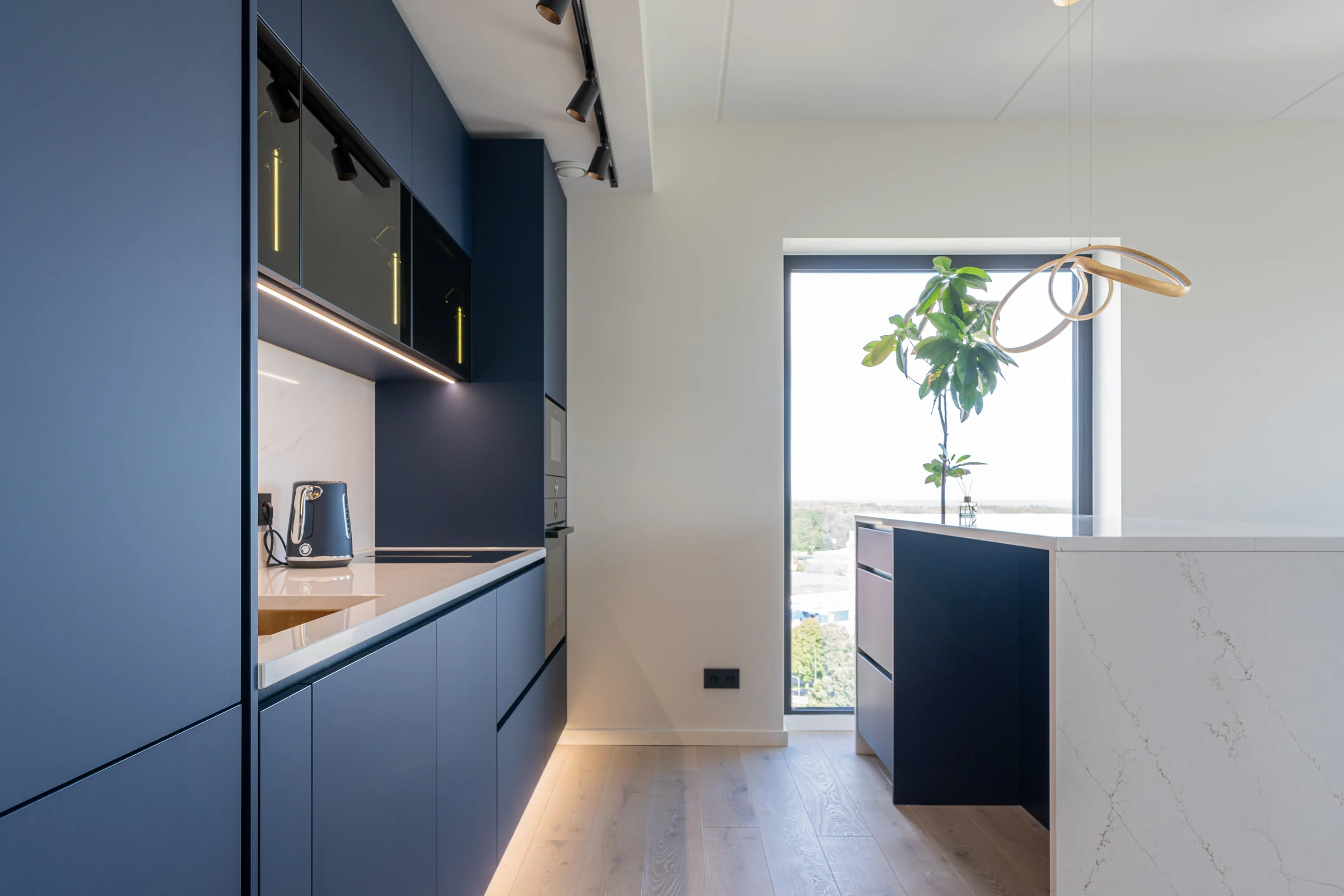 A real kitchen with deep blue matt fronts, light-coloured stone, black appliances and an island